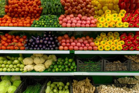 Refrigerated shelves holding various vegetables such as tomatoes, peppers, lettuce, cucumbers and mushrooms